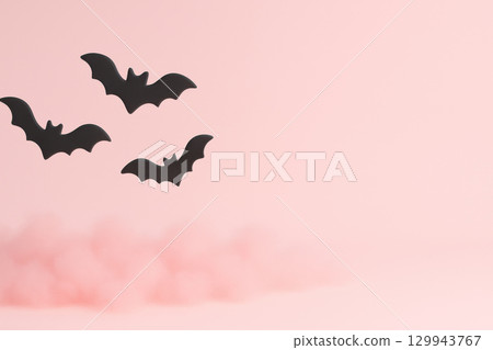 Black bat silhouette flying over soft pink fog with empty pastel background creating spooky Halloween mood 129943767