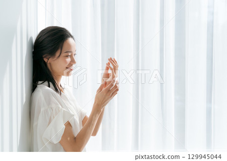 Woman massaging her hands by the window Woman massaging her hands by the window 129945044
