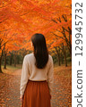 Back view of a woman walking through a forest of autumn leaves 129945732