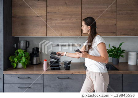 Young woman with healthy diet plan for weight loss, delivery of daily ready meal menu. Woman using meal tracker app on phone. Balanced portion with dish. Pre-cooking. 129946556