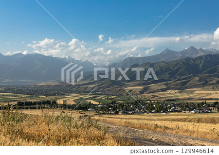 Kyrgyzstan countryside. Agricultural fields near village and mountains. Rural scene, autumn landscape 129946614