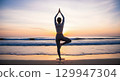 Serene woman practicing yoga tree pose in silhouette on a peaceful sandy beach at sunrise 129947304