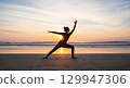 Silhouette of a woman practicing Warrior II yoga pose on a tranquil beach at sunrise or sunset 129947306