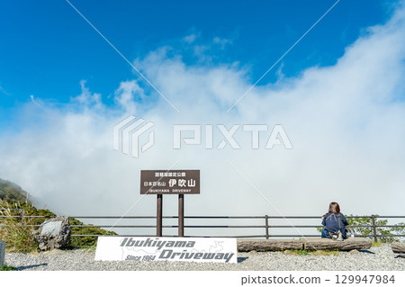 Sekigahara Town, Gifu Prefecture: A sign and a woman holding a dog overlooking the lower world from the Ibukiyama Driveway parking lot. 129947984