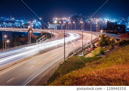 Glowing light trails streaming across zolotoy bridge during nighttime, revealing vibrant cityscape of vladivostok, russia 129948358