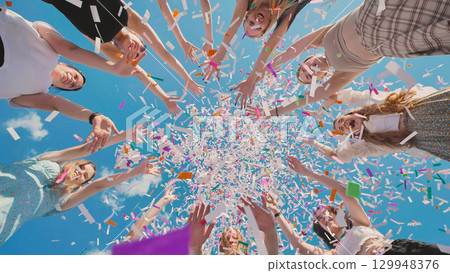 High school graduates joyfully tossing confetti in the air against a backdrop of clear blue sky 129948376