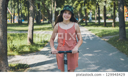 Happy teenager riding electric scooter in a park during summer, enjoying sustainable transportation and outdoor activity Happy teenager riding electric scooter in a park during summer, enjoying sustainable transportation and outdoor activity 129948429