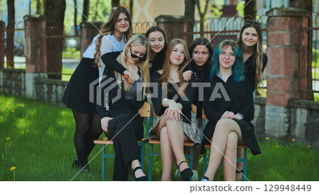Female students gathered on school benches in the schoolyard, savoring their school day together Female students gathered on school benches in the schoolyard, savoring their school day together 129948449
