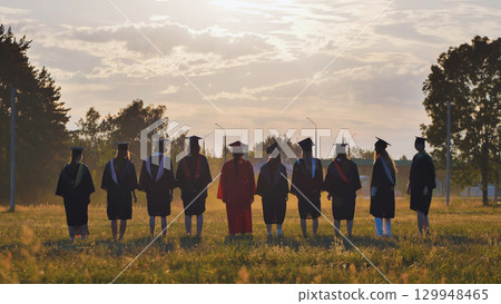 Graduates in academic attire and caps standing in a field at sunset following their graduation Graduates in academic attire and caps standing in a field at sunset following their graduation 129948465