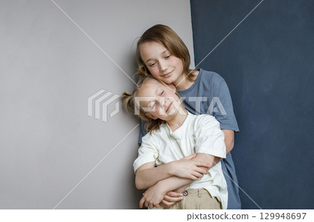 Smiling sibling children having fun at home while standing against blue and white wall background. 129948697