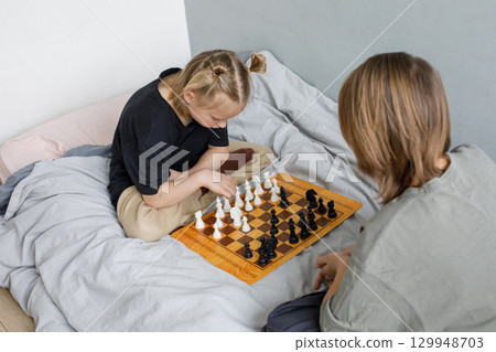 Chess game. Two cute children playing chess at home Chess game. Two cute children playing chess at home 129948703