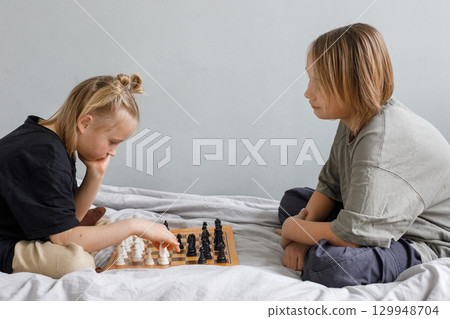 Cheerful boy and girl playing chess board game while thinking of move with knowledge Cheerful boy and girl playing chess board game while thinking of move with knowledge 129948704