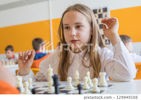 Cheerful child school student on chess lesson indoor. Young girl 10 years old playing chess 129949108