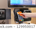 Close-up of woman paying food by tapping credit card at self-checkout counter. 129950017