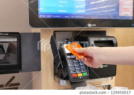 Close-up of woman paying food by tapping credit card at self-checkout counter. Close-up of woman paying food by tapping credit card at self-checkout counter. 129950017
