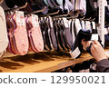 A variety of socks neatly organized on a wooden shelf. A hand is seen comparing two different socks, suggesting a shopper's engagement. 129950021
