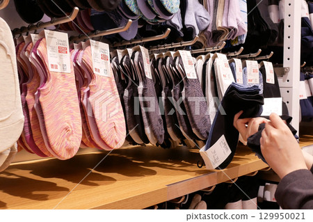 A variety of socks neatly organized on a wooden shelf. A hand is seen comparing two different socks, suggesting a shopper's engagement. 129950021