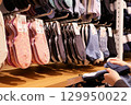 A variety of socks neatly organized on a wooden shelf. A hand is seen comparing two different socks, suggesting a shopper's engagement. 129950022