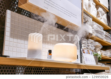 In a cozy retail setting, two essential oil diffusers release gentle streams of mist, creating a calming atmosphere. 129950026