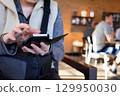Close-up of a woman browsing drink menu on cell phone inside coffee shop 129950030
