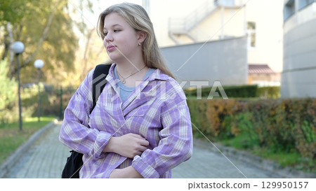A cheerful teenage girl with a bright smile strolls along a green park path. The photo reflects carefree moments and the optimism of adolescence. A cheerful teenage girl with a bright smile strolls along a green park path. The photo reflects carefree moments and the optimism of adolescence. 129950157