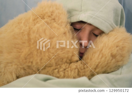 A young boy in a hooded sweater, embracing a soft teddy bear with a peaceful expression. A young boy in a hooded sweater, embracing a soft teddy bear with a peaceful expression. 129950172