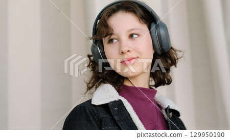 A thoughtful girl wearing headphones appears deeply engaged with her own world. The image symbolizes personal focus, creative thinking, and the emotional connection to sound. 129950190