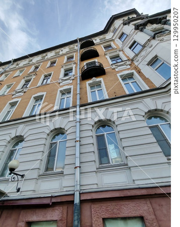 A historic building with ornate stone details, balconies, and an intricate arched entrance featuring a circular window. The image highlights themes of timeless architecture and urban nostalgia. 129950207