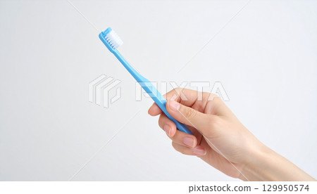 Woman's hand holding a light blue toothbrush and white background 129950574