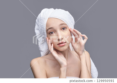 Young caucasian female with towel turban applying eye patches for skincare 129950591