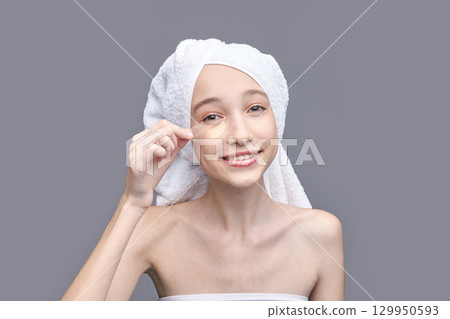 Young caucasian female applying under eye mask in skincare routine with towel 129950593