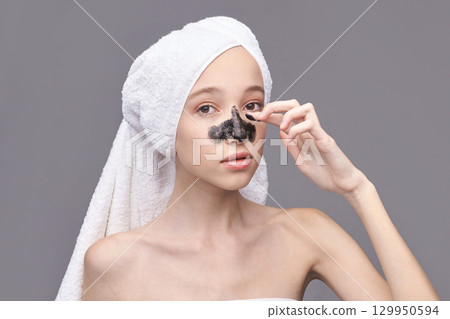 Young caucasian female applying blackhead removal mask with towel wrapped hair Young caucasian female applying blackhead removal mask with towel wrapped hair 129950594