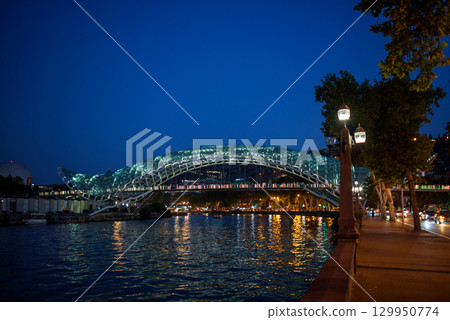 Peace bridge, steel and glass construction pedestrian bridge over Kura Mtkvari river in central Tbilisi, capital of Georgia 129950774
