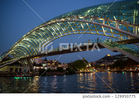 Peace bridge, steel and glass construction pedestrian bridge over Kura Mtkvari river in central Tbilisi, capital of Georgia 129950775