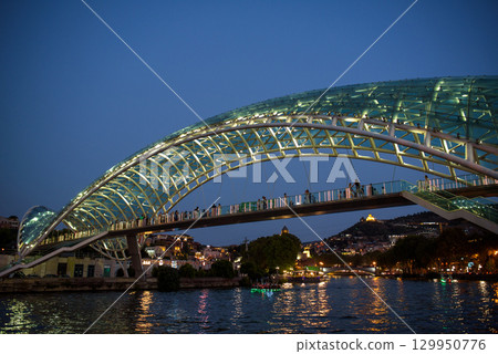 Peace bridge, steel and glass construction pedestrian bridge over Kura Mtkvari river in central Tbilisi, capital of Georgia 129950776
