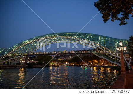 Peace bridge, steel and glass construction pedestrian bridge over Kura Mtkvari river in central Tbilisi, capital of Georgia 129950777