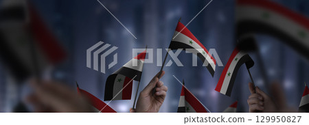 Syria flags in their hands on a blurred urban background 129950827