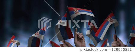 Serbia flags in their hands on a blurred urban background 129950831