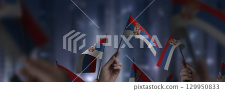 Serbia flags in their hands on a blurred urban background 129950833