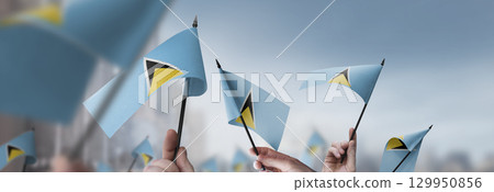 Saint Lucia flags in their hands on a blurred urban background Saint Lucia flags in their hands on a blurred urban background 129950856