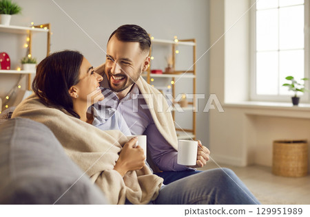 Happy laughing couple in love sitting on sofa at home with a cup of tea and looking at each other Happy laughing couple in love sitting on sofa at home with a cup of tea and looking at each other 129951989