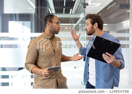Two colleagues having a heated discussion in a modern office setting, expressing dissatisfaction. Two colleagues having a heated discussion in a modern office setting, expressing dissatisfaction. 129954798