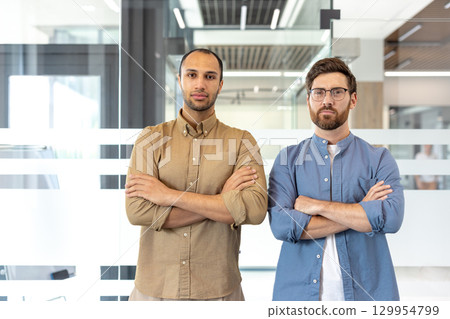 Two professional individuals standing confidently in a modern office setting, conveying leadership and teamwork. 129954799