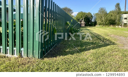 Green metal fence along grass field under blue sky 129954893