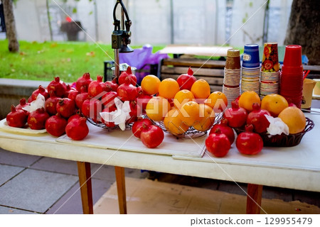 Fresh fruits including pomegranates and oranges with a table press juicer machine in a street in Tbilisi, Georgia 129955479