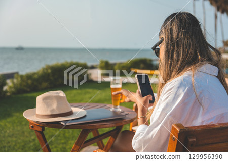 A woman is sitting at a table by the ocean, remote work concept 129956390