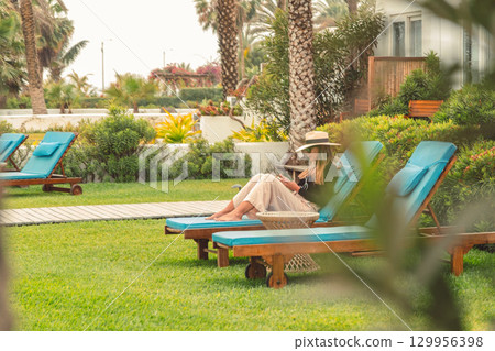 A woman is sitting on a blue lounge chair in a lush beach house A woman is sitting on a blue lounge chair in a lush beach house 129956398