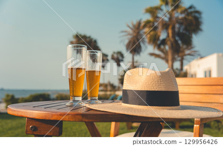 A table with two glasses of beer and a straw hat on it A table with two glasses of beer and a straw hat on it 129956426