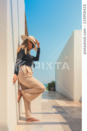 A woman wearing a straw hat stands on a white wall A woman wearing a straw hat stands on a white wall 129956428