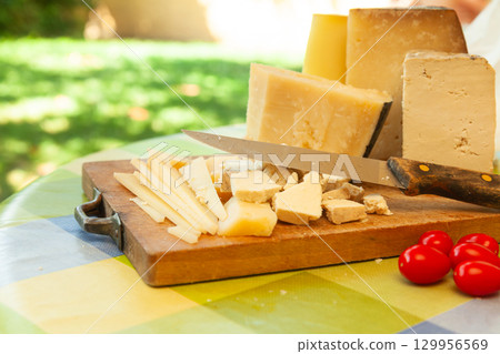 Hard cheese assortment with knife and red tomatoes on table in garden setting Hard cheese assortment with knife and red tomatoes on table in garden setting 129956569